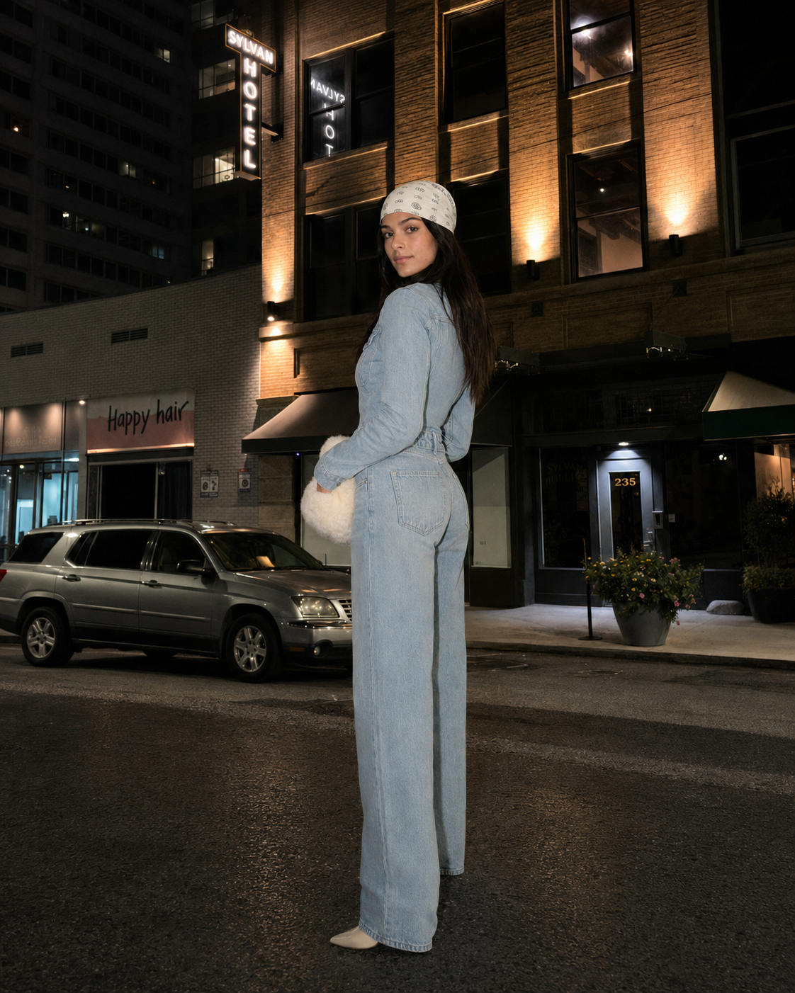 Woman in a light denim jumpsuit looking back on a city street at night
